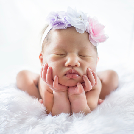 Newborn 7 day old baby girl on his white bed relaxing and flower on her headの写真素材