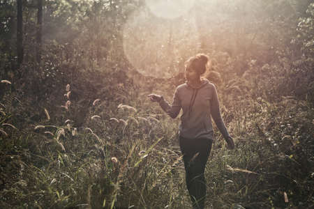 A young woman walking trekking through a green path in forest mountain summer sunrise thailand.の写真素材