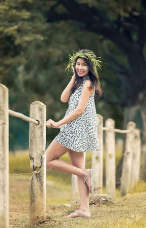 beautiful fairy:pretty girl in grass crown and makeup posing gracefully on green outdoors and  fence copy space tree backgroundの写真素材