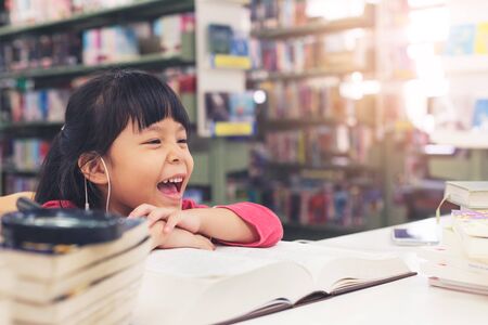 Cute little children girl pink cloth smiling studying at the library and book on shelf backgroundの写真素材