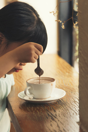 A cute little children girl drinking hot chocolate in cafe shopの写真素材