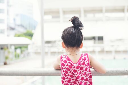 asia children girl in 6 years old wearing pink dress looking to swimming pool view on summer at bangkok, Thailand. travel conceptの写真素材
