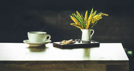 Coffee drink on wooden table with blur cafeteria brick background. white cup of coffee with sweet biscuit bakery and grass on table in cafe, Morning lightの写真素材