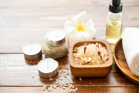 Sea salt, towels, aroma oil in bottles and flowers on vintage wooden background. Selective focus.