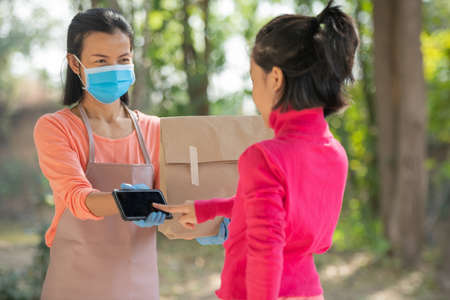 delivery, mail, people and shipping concept.Young woman sign in digital mobile phone after receiving parcel from courier at home. from delivery man during COVID-19 outbreak.の写真素材