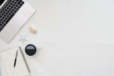Flat lay photo of office desk with laptop, notebook, pen, coffee, starfish and shells with copy space backgroundの写真素材