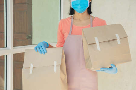 postman, delivery man wearing mask carry small box deliver to customer in front of door at home. woman wearing mask prevent covid 19, coronavirus infection outbreak. home delivery shopping concept.の写真素材