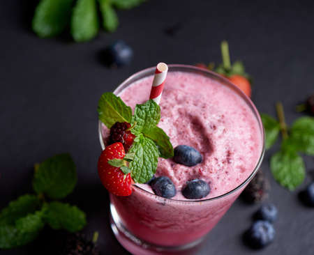 Delicious strawberry, mulberry and blueberry smoothie garnished with fresh berries and mint in glass. soft focus. beautiful appetizer pink raspberries, well being and weight loss concept.の写真素材