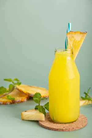 Pineapple cocktail or fresh pineapple juice, mint leaves in glass bottles with straws with ice and ...