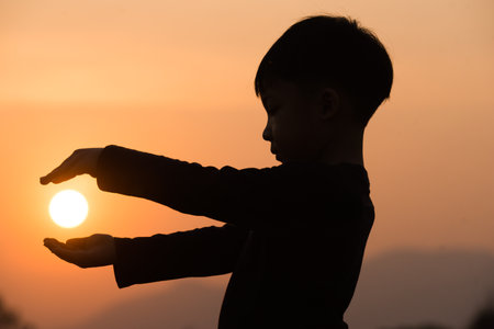 A boy playing with the sun at sunset. Silhouette picture with orange sunset sky.