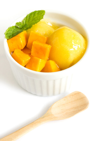 Mango ice cream in a white bowl on white background. Decorate with mint leaf slided mango and wood spoon.の写真素材