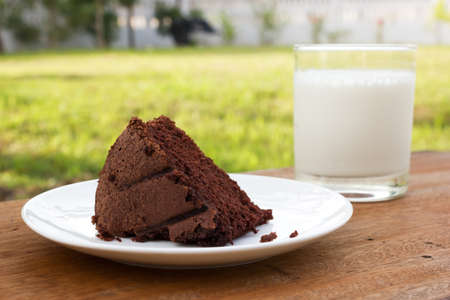 Chocolate cake on white plate. Put on wood table Selected focus on front. A glass of milk and garden  view are background.の写真素材
