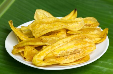 Fried banana chips on white plate with banana leaf background.の写真素材
