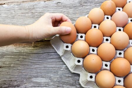 Woman's hand picking egg from egg tray. On wooden background. Top view.