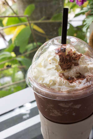Closeup chocolate frappe  in a plastic cup, topped with whipped cream. It is on a  glass  table.の写真素材