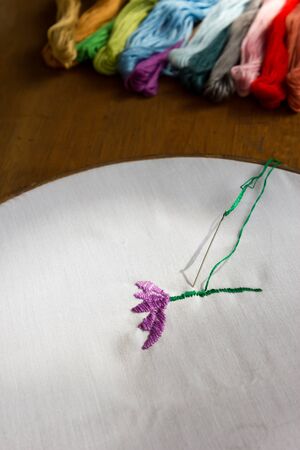 Incomplete embroidery  (purple flower) and embroidery craft tools on wooden background. With...