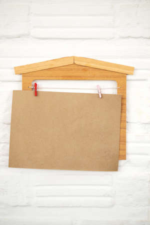 Blank brown paper hanging with house wooden decorate on white wall. Concept background. Copy space.の写真素材