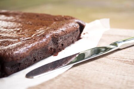 Closeup side of brownie. Knife nearly and shadow light. Dessert background. Sweet and moist chocolate dessert. Over wooden table.の写真素材