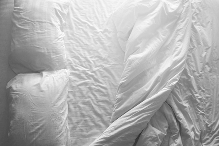 Messy double bed. Two pillows and blanket on white cover sheets. Top view. Black and white theme. Indoor and house object background. With light filter effect.の写真素材