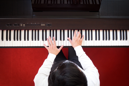 Asian man playing piano. Top view with red floor background. Favorite music instrument for learning basic of rhythm and music skill. Art background.の写真素材