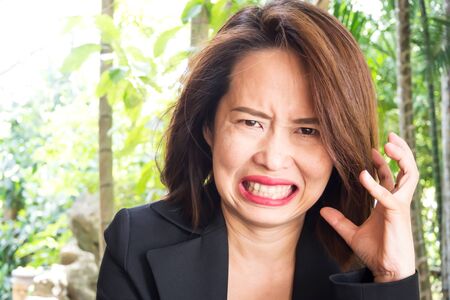 Business asian woman dissatisfied face. Ugly grin and with angry feeling. 30s with brown hair and black suit. Nagative emotion.の写真素材