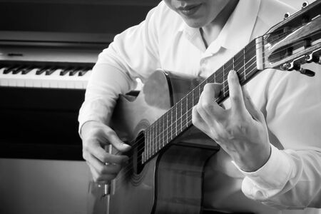 Closeup young Asian man play guitar with piano background. Classical music instrument. String...