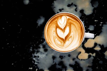 Latte art of two heart in white cup. Dirty spill coffee on black background. Top view.の写真素材