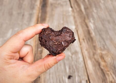 Woman holding brownie of heart shape. Wooden background. Favorite chocolate dessert. Richy tasty of chocolate.の写真素材