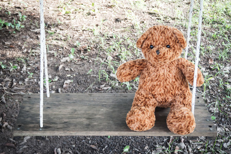 Brown teddy bear sitting on swing. Feeling alone. Favorite doll of childhood.の写真素材