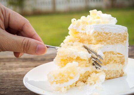 Woman hand using fork cut vanilla sponge cake with cream and white chocolate decorate. Sliced piece...