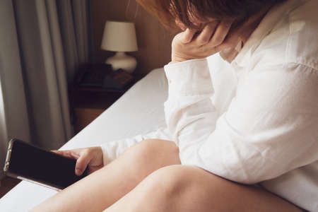Asian woman playing smart phone on bed. Concept of feel lonely. Vintage and pastel color tone.の写真素材