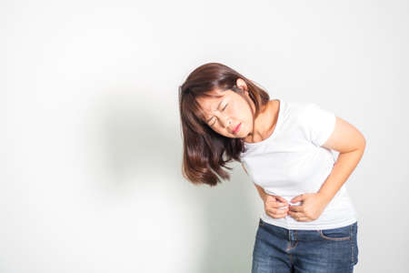 Asian adult woman stomachache. Symptom of Period cramps. Hand holding tummy. Portrait on white background with copy space.の写真素材