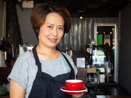 Asian adult waitress holding empty red cup. . Concept of keep cleaning cup.の写真素材