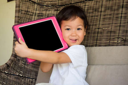 Smiling Asian little girl holding tablet on her hands. Concept of happiness time with technology and child on situation online learning.の写真素材