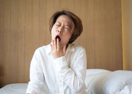 Asian middle adult woman yawning on bed. Concept of tried from overwork.の写真素材