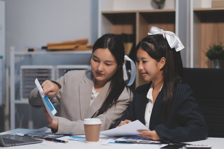 Two young Asian business woman talk, consult, discuss working with new startup project idea presentation analyze plan marketing and investment in the office.の写真素材