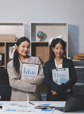 Two young Asian business woman talk, consult, discuss working with new startup project idea presentation analyze plan marketing and investment in the office.の写真素材