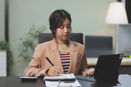telework concept - Asian business woman uses laptop computer to join video meeting and writes notes on her digital tablet at homeの写真素材