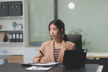 telework concept - Asian business woman uses laptop computer to join video meeting and writes notes on her digital tablet at homeの写真素材