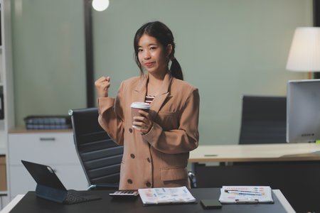Happy Asian businesswoman working for her project and drinking coffee cup while working, sitting at the office desk.の写真素材