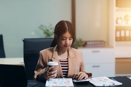 Happy Asian businesswoman working for her project and drinking coffee cup while working, sitting at the office desk.の写真素材
