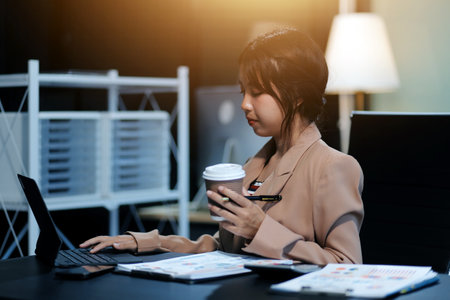 Happy Asian businesswoman working for her project and drinking coffee cup while working, sitting at the office desk.の写真素材