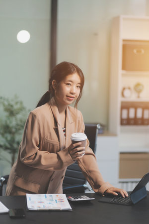 Happy Asian businesswoman working for her project and drinking coffee cup while working, sitting at the office desk.の写真素材