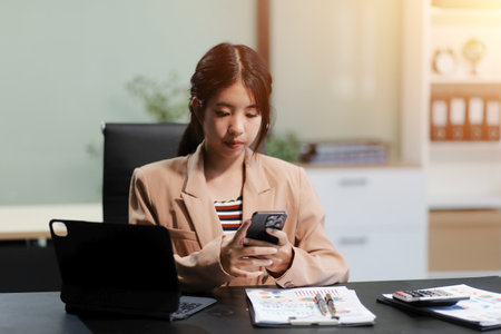 Asian Woman entrepreneur busy with her work in the office. Young Asian woman talking over smartphone or cellphone while working on computer at her desk.の写真素材
