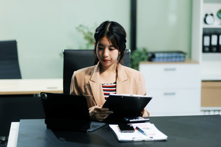 telework concept - Asian business woman uses laptop computer to join video meeting and writes notes...