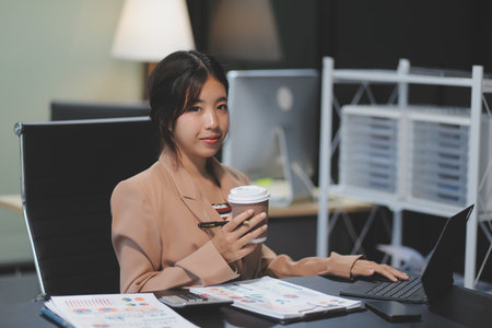 Happy Asian businesswoman working for her project and drinking coffee cup while working, sitting at the office desk.の写真素材