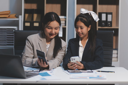 Two young Asian business woman talk, consult, discuss working with new startup project idea presentation analyze plan marketing and investment in the office.の写真素材
