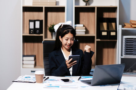 Excited happy Asian woman looking at the phone screen, celebrating an online win, overjoyed young asian female screaming with joy, isolated over a white blur backgroundの写真素材