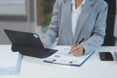 Asian Businesswoman Using laptop computer and working at office with calculator document on desk, doing planning analyzing the financial report, business plan investment, finance analysis concept.の写真素材