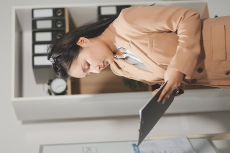 Asian Businesswoman Using laptop computer and working at office with calculator document on desk, doing planning analyzing the financial report, business plan investment, finance analysis concept.の写真素材
